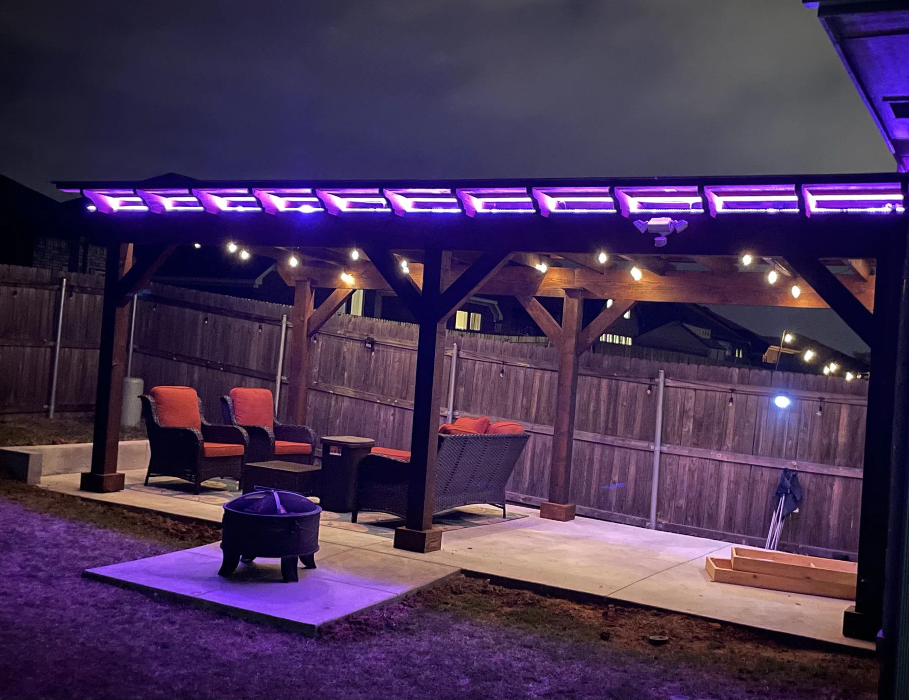 Purple LED pergola with string lights and fire pit — outdoor evening living